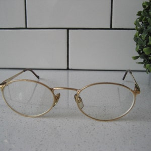 May include: Gold-tone oval-shaped eyeglasses with clear lenses.