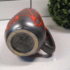 K&ouml;nnte beinhalten: Schwarze Keramikvase mit roter Glasur, die ein einzigartiges Tropfdesign aufweist. Die Vase hat einen runden Boden und einen Henkel.