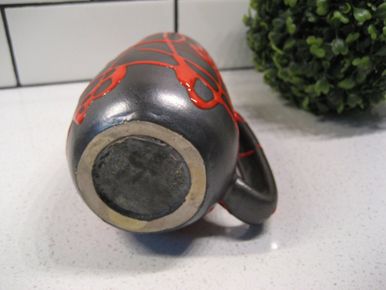 K&ouml;nnte beinhalten: Schwarze Keramikvase mit roter Glasur, die ein einzigartiges Tropfdesign aufweist. Die Vase hat einen runden Boden und einen Henkel.