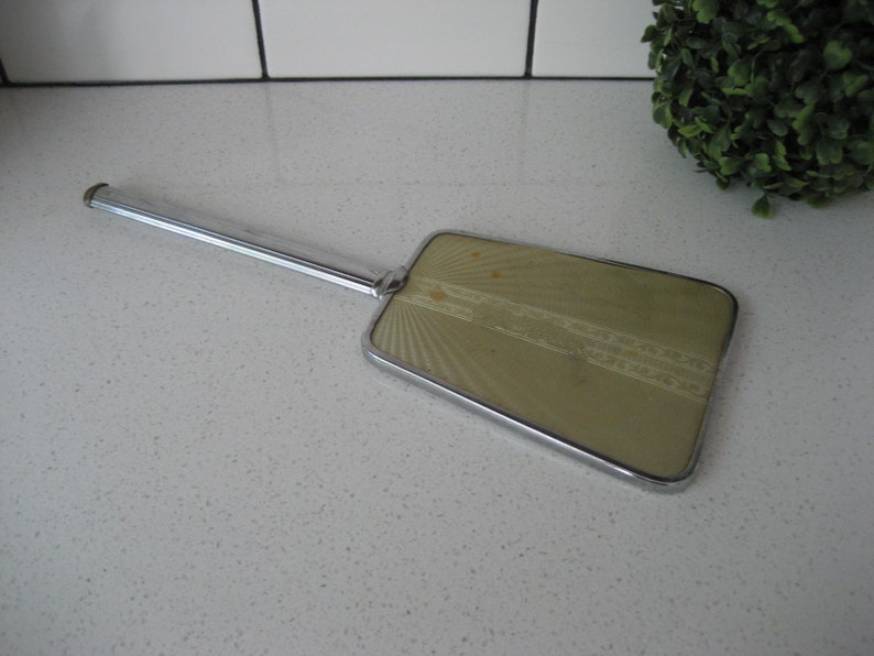 May include: A vintage hand mirror with a silver handle and a rectangular, green-tinted glass mirror with a decorative pattern.