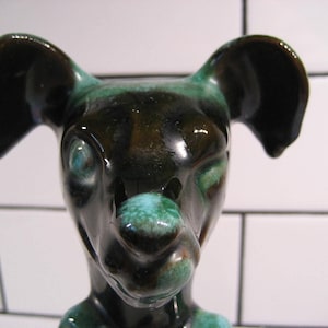 Puede incluir: Una figurita de perro de cerámica con esmalte negro y verde. El perro tiene orejas grandes y un hocico largo.