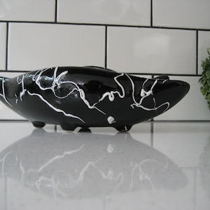 Könnte beinhalten: Schwarze Keramikschale mit weißen Marmorierungen. Die Schale ist bootförmig und hat einen abgerundeten Boden.