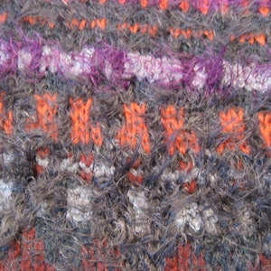 May include: Close-up of a fuzzy, multi-colored knitted fabric with stripes of orange, purple, white, and gray.