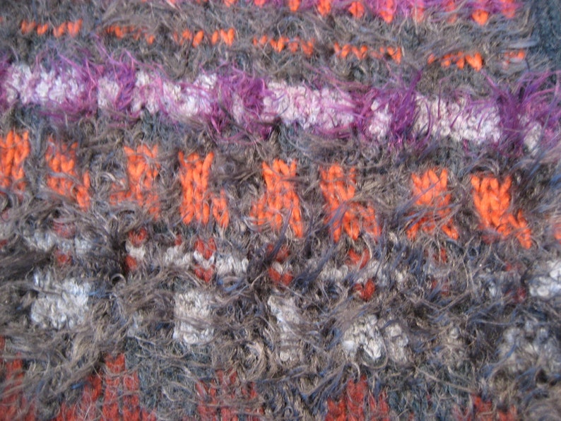 May include: Close-up of a fuzzy, multi-colored knitted fabric with stripes of orange, purple, white, and gray.