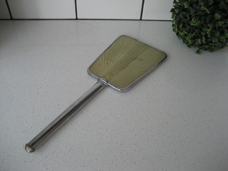 May include: A vintage hand mirror with a silver handle and a green, fan-shaped mirror with a decorative pattern.