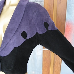 Op de afbeelding: Een paars en zwart suède jack met een reverskraag en lange mouwen. Het jack heeft een uniek ontwerp met een paars suède paneel aan de voorkant en zwart suède aan de achterkant en mouwen.