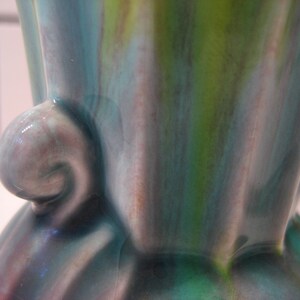 May include: A ceramic vase with a green, blue and purple glaze. The vase has a unique, organic shape with a curved handle.