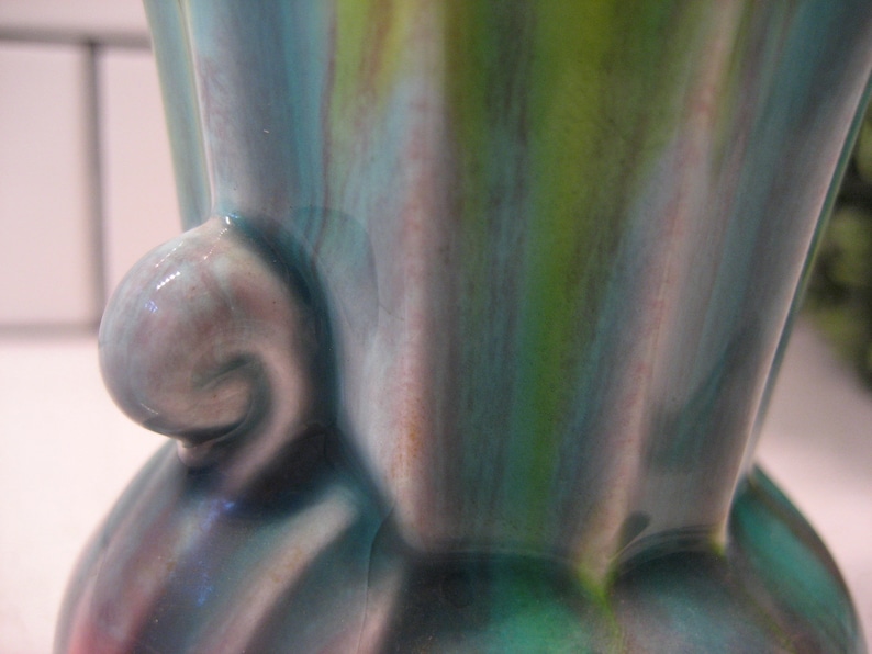 May include: A ceramic vase with a green, blue and purple glaze. The vase has a unique, organic shape with a curved handle.