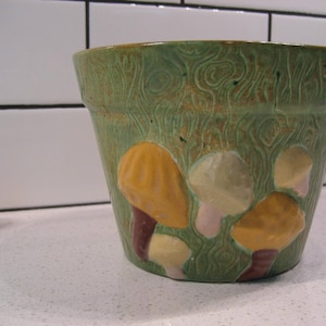 May include: A green ceramic planter with a woodgrain pattern and yellow, brown, and white mushroom designs.