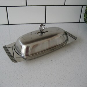 May include: A silver butter dish with a lid and a decorative ring handle. The dish has a textured edge.