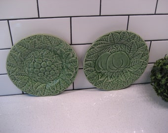 Puede incluir: Dos platos de cerámica verde con diseños en relieve de hojas y frutas. Los platos están sobre una superficie de azulejos blancos.