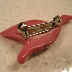 May include: A pink ceramic brooch in the shape of a bird with a silver pin and clasp.
