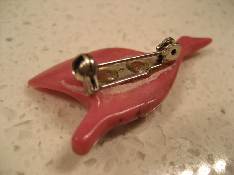 May include: A pink ceramic brooch in the shape of a bird with a silver pin and clasp.