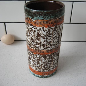 Peut inclure: Un vase en céramique brun, blanc et orange avec un motif texturé. Le vase a une large ouverture et une forme cylindrique.