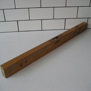 May include: A wooden level with a brass level indicator. The level is approximately 60 cm long.