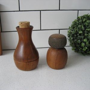 Puede incluir: Dos saleros y pimenteros de madera con tapas de corcho. El salero es redondo y rechoncho, mientras que el pimentero es más alto y delgado. Ambos saleros tienen un acabado de madera marrón oscuro.