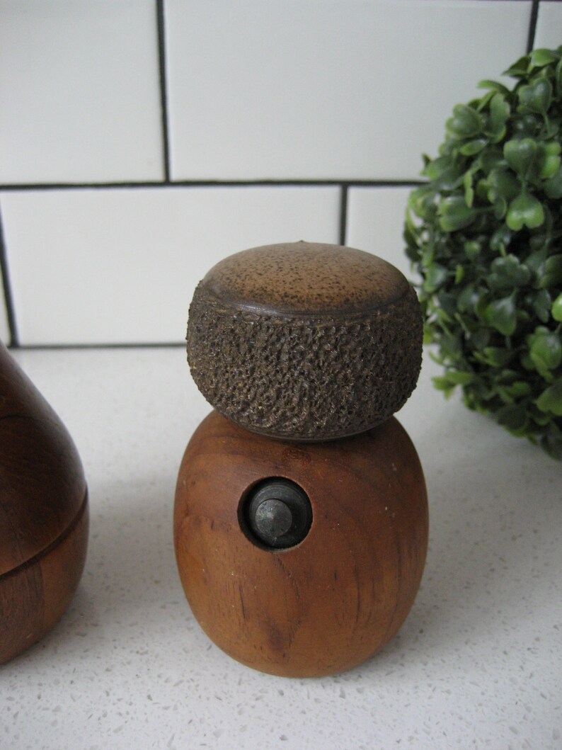 K&ouml;nnte beinhalten: Ein Set aus zwei Salz- und Pfefferstreuern aus Holz mit einer strukturierten Oberseite und einem kleinen Metallknopf an der Unterseite.