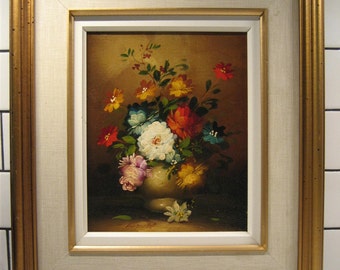 May include: Oil painting of a floral still life in a gold frame. The artwork features a vase overflowing with colorful flowers in shades of red, white, blue, yellow, and pink. The frame has a gold outer edge and a white inner border.