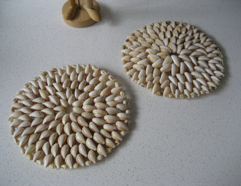 May include: Two round coasters made of white seashells arranged in a circular pattern. The coasters are on a white surface.