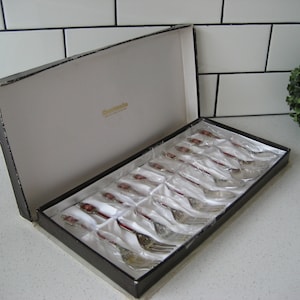 May include: A set of 12 silver-plated teaspoons with red and gold handles in a black box. The box has the word "Remarkable" printed on it.