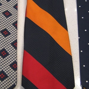 May include: A navy blue tie with orange and red stripes. The tie has a textured surface.
