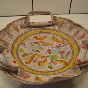 Op de afbeelding: Een wit keramisch dienblad met twee handvatten en een bloemenmotief in tinten geel, oranje, rood, groen en blauw. Het dienblad heeft een gekrakelde glazuurfinish.