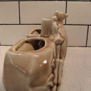 Może przedstawiać: Ceramiczna doniczka w kształcie wielbłąda z dwoma oddzielnymi doniczkami na grzbiecie. Doniczka jest jasnobrązowa z błyszczącym wykończeniem.