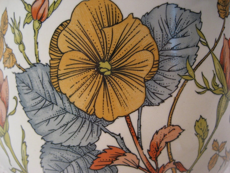 May include: A vintage ceramic plate with a floral design featuring a large yellow flower with orange accents and gray leaves.