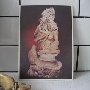 Może przedstawiać: Rzeźba z drewna przedstawiająca kobietę z rozwianym włosem i ptakiem siedzącym na jej ramieniu. Rzeźba jest pomalowana w odcieniach brązu i bieli, z czerwonym akcentem na skrzydle ptaka.