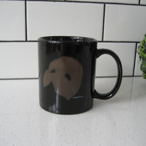 May include: Black ceramic coffee mug with a brown phantom of the opera mask graphic.