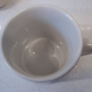May include: A white ceramic mug with a rounded handle. The mug is empty and appears to be new.