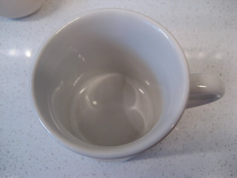 May include: A white ceramic mug with a rounded handle. The mug is empty and appears to be new.