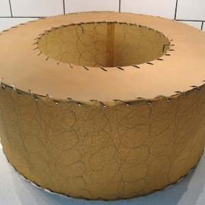 May include: A brown paper lampshade with a stitched edge and a leaf pattern. The lampshade is round and has a hole in the center.