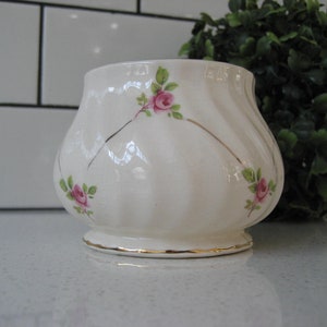 May include: A white ceramic sugar bowl with a gold rim and pink rose floral design.