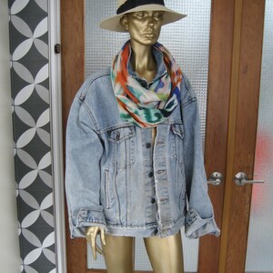 Könnte beinhalten: Eine hellblaue Jeansjacke mit einem bunten Schal und einem Strohhut. Die Jacke hat einen Knopfverschluss und lange Ärmel.