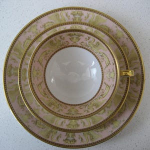 May include: A set of three pink and gold porcelain teacups and saucers with a decorative pattern of stylized birds and floral motifs.
