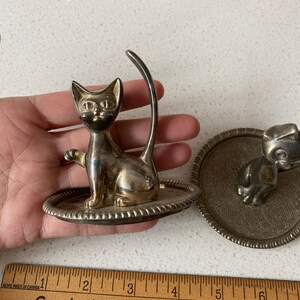 K&ouml;nnte beinhalten: Zwei silberne Ringhalter, einer in Form einer Katze und der andere in Form eines Hundes. Beide Halter haben eine kleine Schale, um den Ring zu halten.