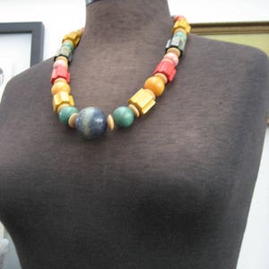 May include: A colorful wooden bead necklace with a blue and green bead in the center. The necklace is on a black mannequin.