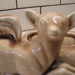 Może przedstawiać: Ceramiczna doniczka w kształcie jelenia z dwoma mniejszymi doniczkami na grzbiecie. Jeleń jest jasnobrązowy, a doniczki są nieco ciemniejsze.