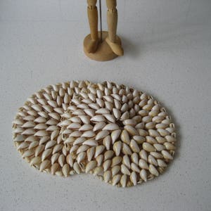 May include: Two round coasters made of white seashells arranged in a circular pattern. The coasters are on a white surface.