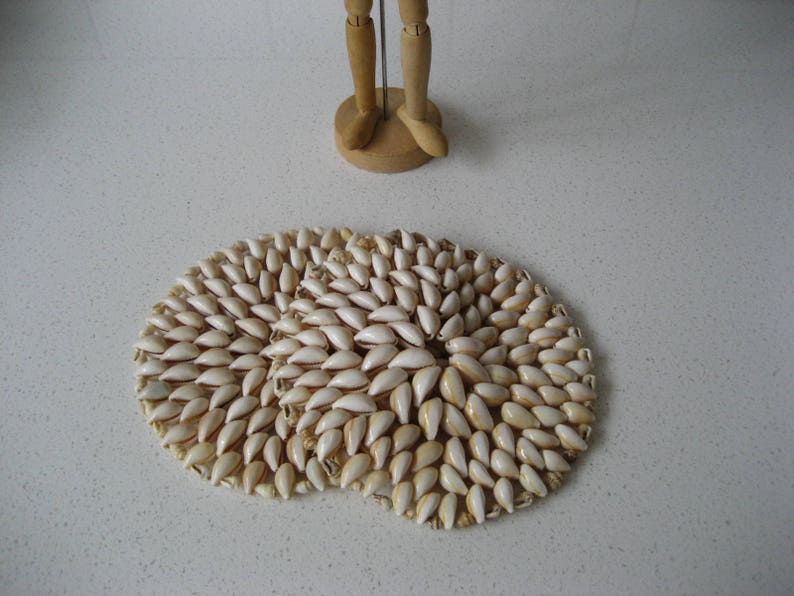 May include: Two round coasters made of white seashells arranged in a circular pattern. The coasters are on a white surface.