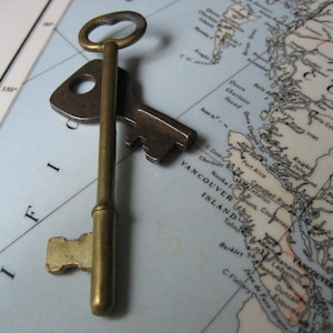 May include: A vintage brass key with a large, ornate head and a long, slender shaft. The key is lying on a map of Vancouver Island, British Columbia, Canada.