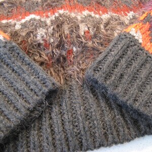 May include: A close-up of a gray knitted sweater with orange and white stripes. The sweater has a fuzzy texture and is made of a thick yarn.