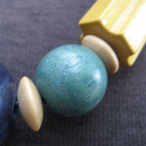 May include: A close-up of a necklace made of wooden beads. The beads are blue, green, and cream colored. The beads are round and have a smooth finish.
