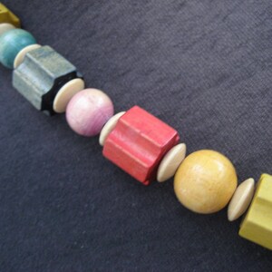 May include: A colorful wooden bead necklace with yellow, green, brown, pink, red, and beige beads. The beads are various shapes and sizes.