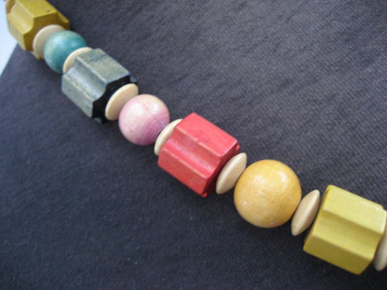 May include: A colorful wooden bead necklace with yellow, green, brown, pink, red, and beige beads. The beads are various shapes and sizes.