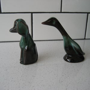 May include: Two ceramic figurines, a black and green dog and a black and green duck, on a white countertop.
