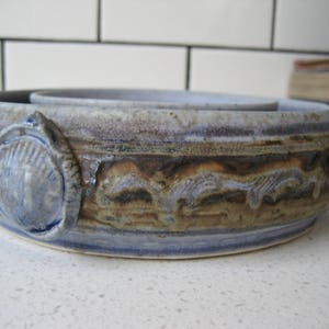May include: A ceramic serving bowl with a blue and brown glaze. The bowl has a decorative design of seashells and other ocean-inspired motifs.