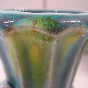May include: A blue and green ceramic vase with a wavy, abstract design. The vase has a wide mouth and a narrow base.