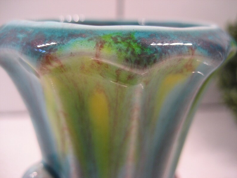 May include: A blue and green ceramic vase with a wavy, abstract design. The vase has a wide mouth and a narrow base.